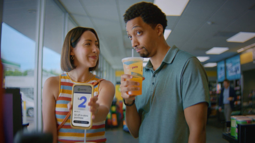 a couple standing in a convenient store holding a phone and drink