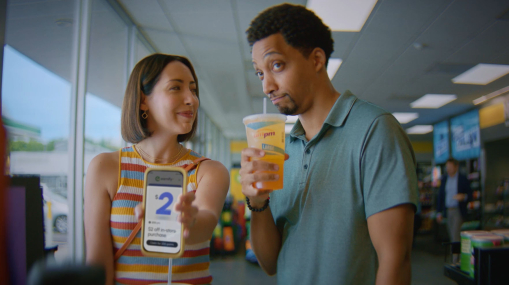 a couple standing in a convenient store holding a phone and drink